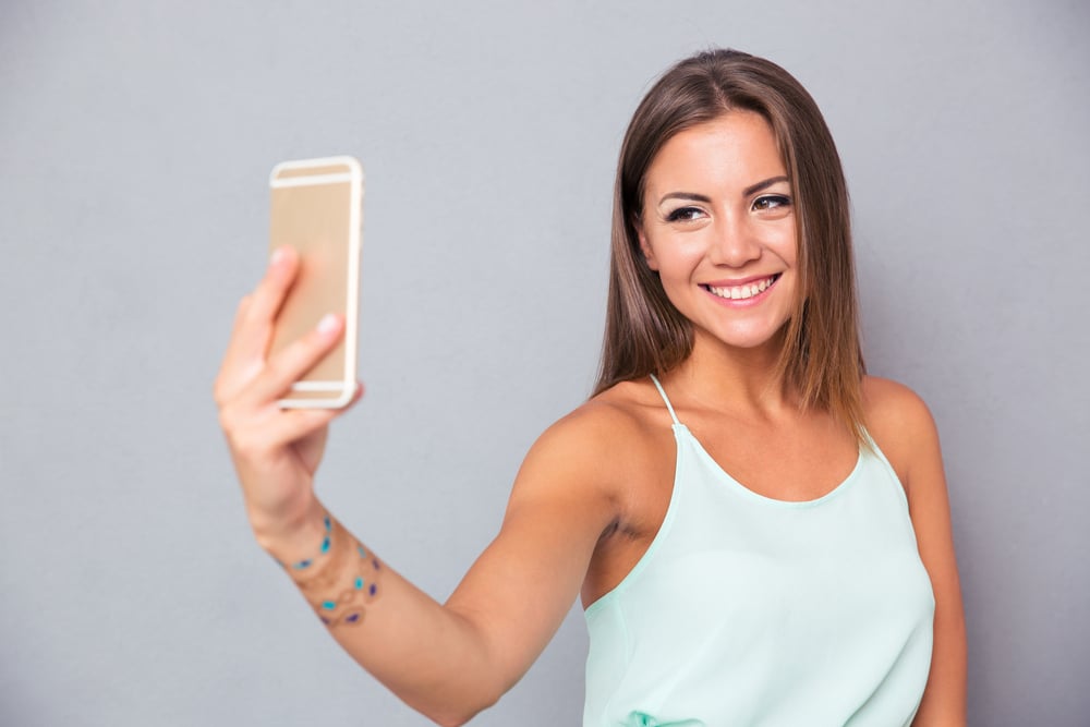 Smiling young girl making selfie photo on smartphone over gray background